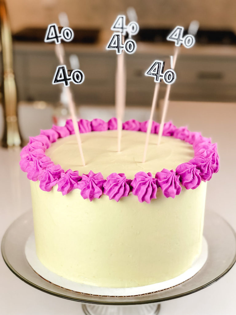Triple Layer Huckleberry and White Cake with White Chocolate Frosting with tall candles.  There are six  candles, which have the numerals, "40" in black.  The frosting is white chocolate buttercream with purple accent color around the top of the cake.