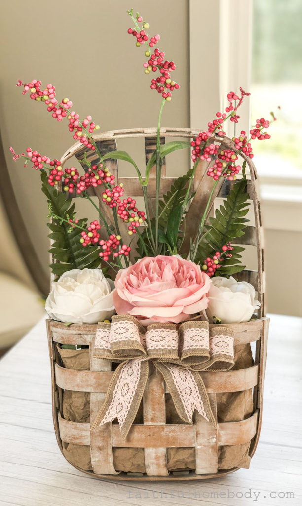 How to Make a Hanging Tobacco Basket for Valentine's Day is displayed.  Pink and white peonies with pink, red, and white berry stem and fern leaves.  A burlap and pink lace bow is attached to the front of the tobacco basket.