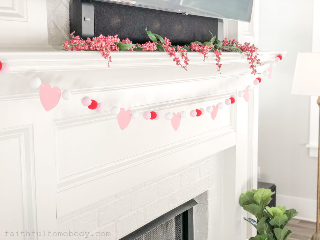 Red, pink, and white pom pom garland displayed on a mantle. There are small pink hearts between the pom poms.