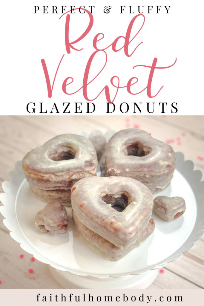 Homemade Red Velvet Glazed Donuts  stacked on a white scalloped stand.  The donuts are heart shaped.  Pink confetti surrounds the stand.