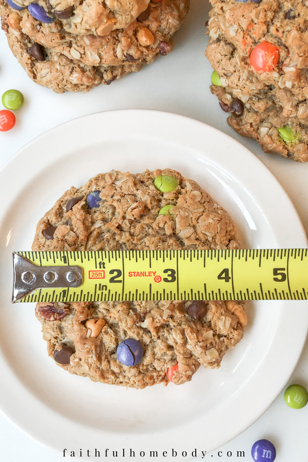 A big cookie is placed on a white plate.  A measuring tape spans across the cookie, measuring 4 inches.  Cookies are in the background, surrounding the plate.