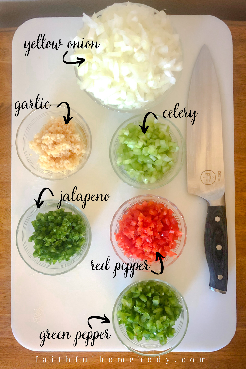 Small, clear bowls are filled with chopped onion, minced garlic, diced celery, diced red and green bell peppers, diced celery, and diced jalapeno.  They are placed on a large white cutting board with a large knife placed on the right side of the board.  